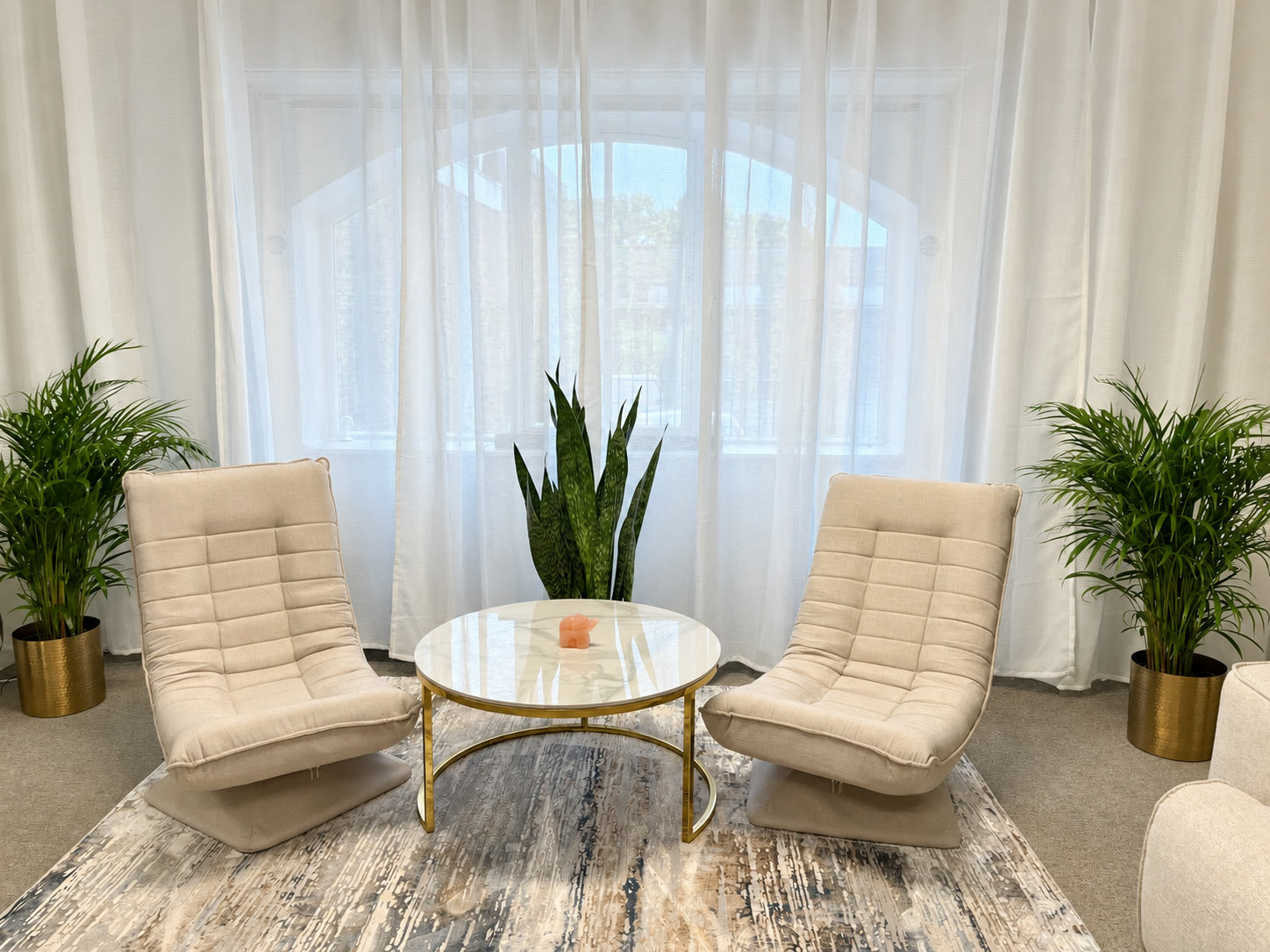 Two cream chairs and a round table by the arched window in reception