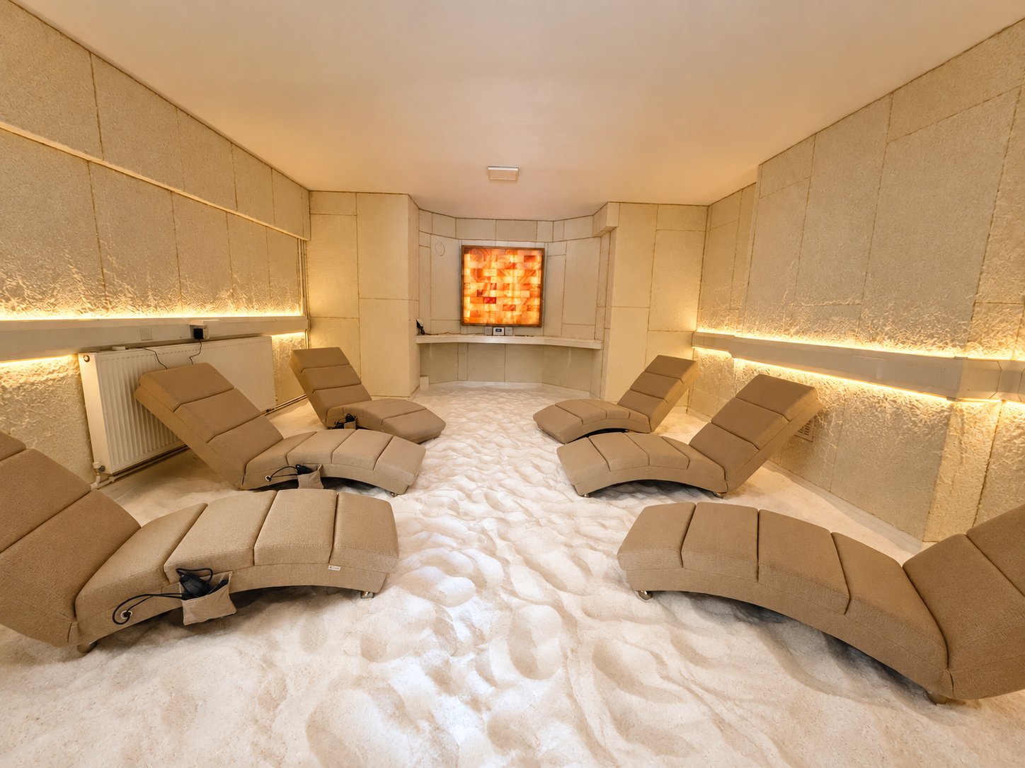 The salt room: cream recliners on a deep bed of white salt, with the backlit Himalayan salt panel