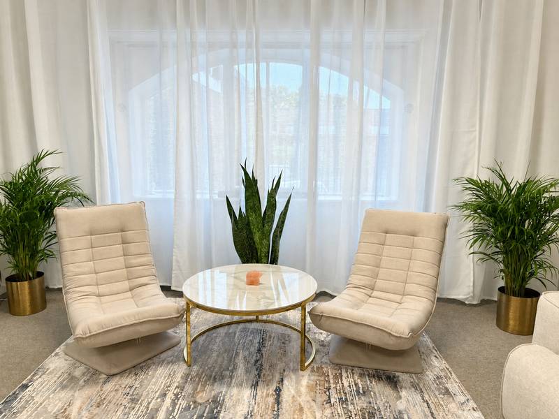 Two cream chairs and a round table by the arched window in reception